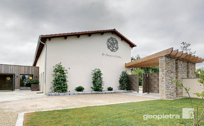 Main entrance of a building featuring the use of Geopietra manufactured stone, with a wooden pergola and a well-maintained garden