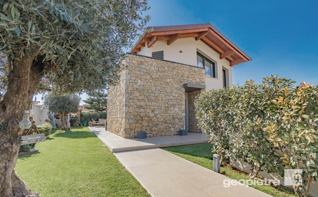Exterior facade of a modern house enhanced by the use of Geopietra manufactured stone, surrounded by a lush and well-maintained garden.